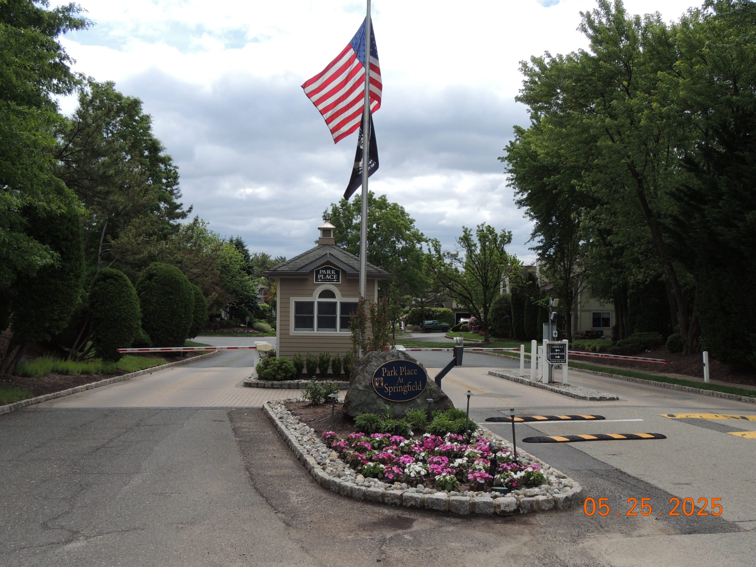 A gated entrance with a small guardhouse, American flag, flower bed, and a sign reading "Park Place Spring Lake"; date on photo is May 25, 2025.